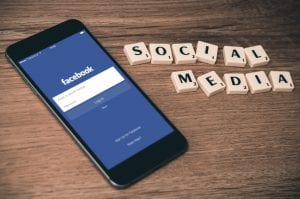Smartphone with Facebook login on screen, sitting on table with Scrabble tiles spelling &ldquo;Social Media;&rdquo; image by William Ivey, via Unsplash.com.