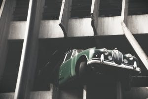 Green car extending outside parking garage after hitting barrier; image by Carafife, via Unsplash.com.