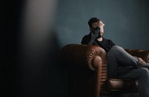 Man sitting on sofa resting his head in his hand; image by Nik Shuliahin, via Unsplash.com.