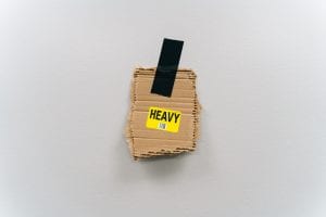 Piece of cardboard with &ldquo;Heavy&rdquo; sticker on it taped to neutral wall with black tape; image by Keagan Henman, via Unsplash.com.