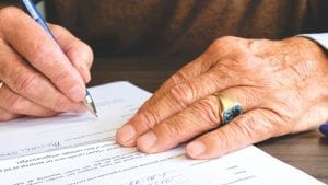 Man signing paperwork; image via Pexels.com.