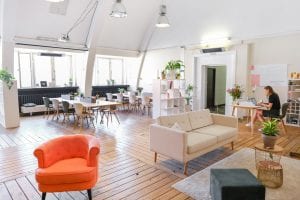 Open floor plan apartment, woman working on laptop at table; image by CoWomen, via Unsplash.com.