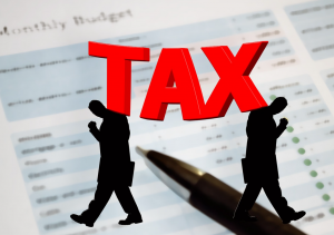 Budget paper and pen with silhouettes of two men walking away from each other and the word &ldquo;Tax&rdquo; in bold red letters; image by Geralt, via Pixabay.com.