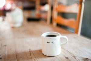 White mug of coffee with &ldquo;Begin&rdquo; written on it; image by Danielle MacInnes, via Unsplash.com.