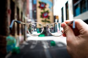 Man holding pair of glasses, surrounding scenery blurry; image by Josh Calabrese, via Unsplash.com.