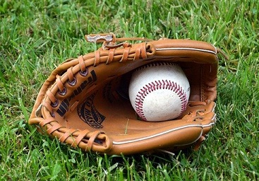 A baseball rests inside of a leather mitt, on grassy ground.