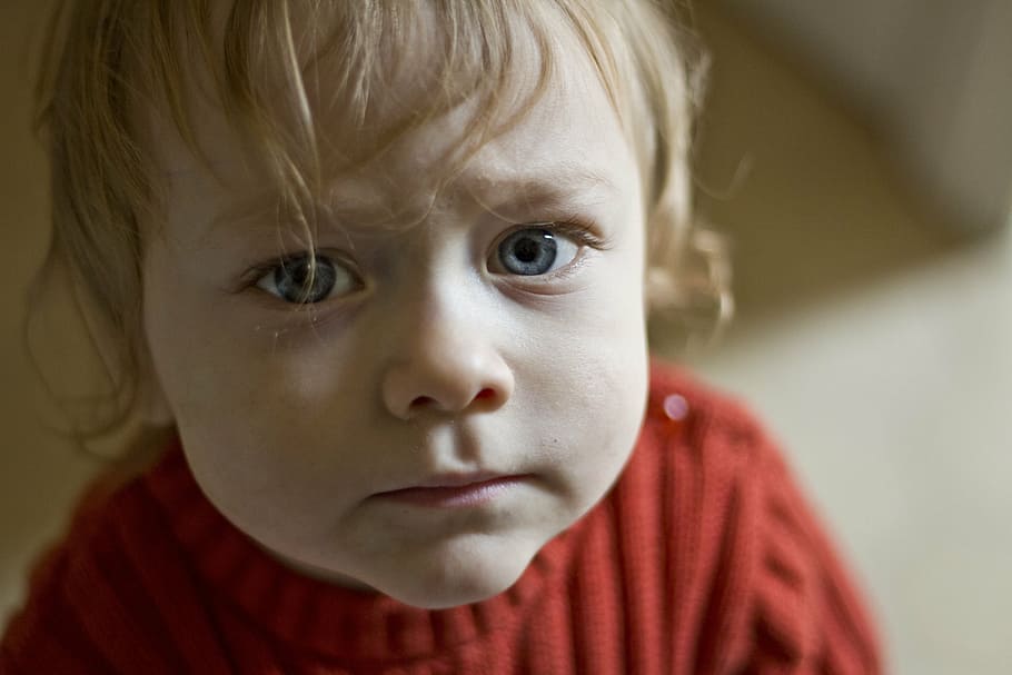 A toddler in a red sweater looks sad.