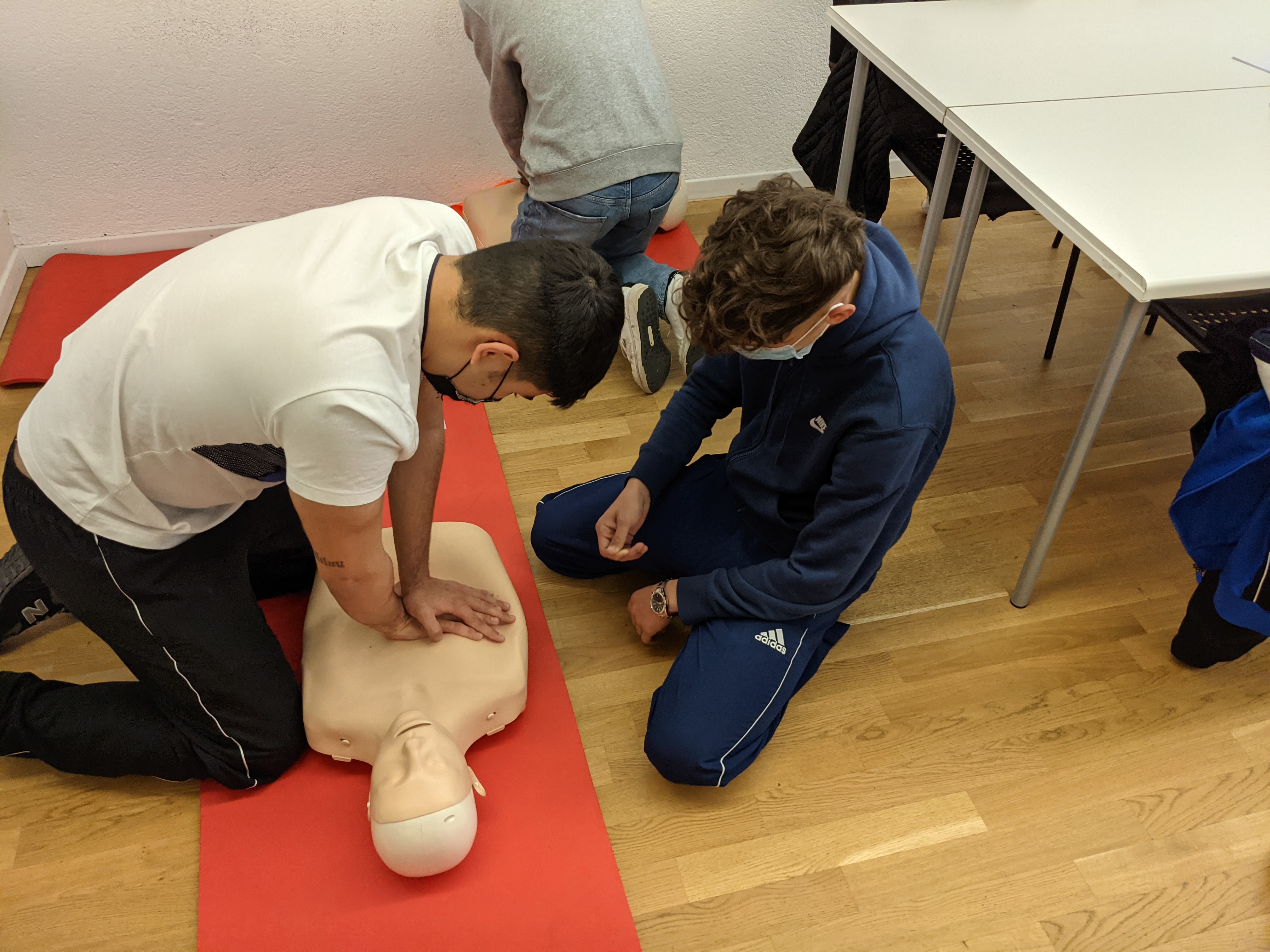 Two men performing CPR on practice manequin; image by Martin Splitt, via. Unsplash.com.