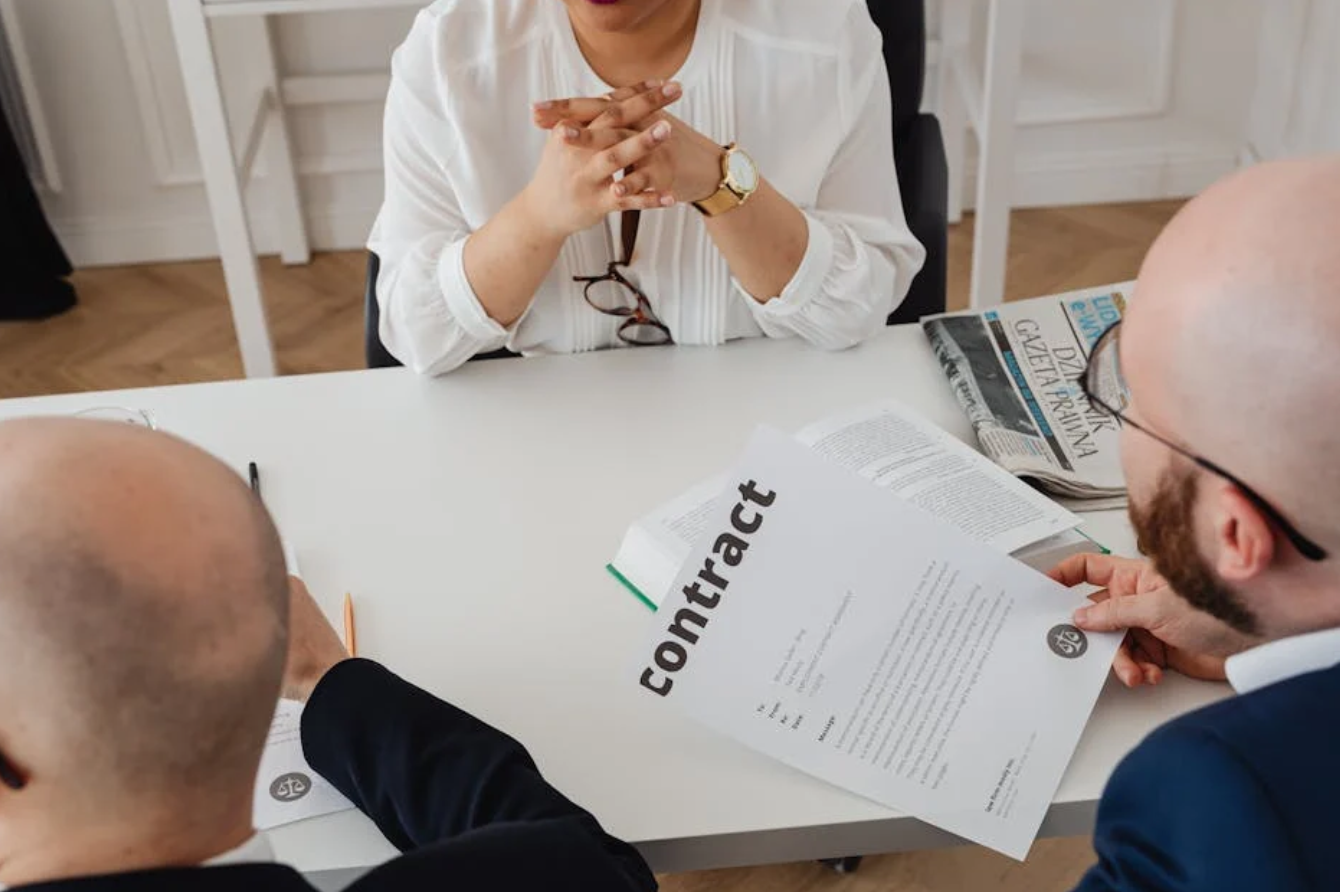 Two men and one woman discussing a contract; image by Karolina Grabowska, via Pexels.com.
